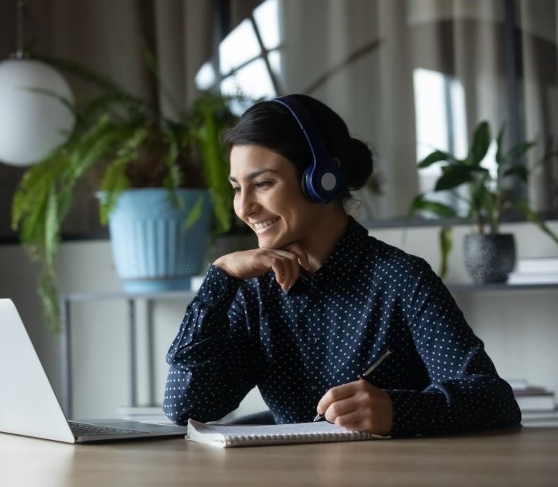 msc business analytics admissions, edhec online. Happy young indian girl with wireless headphones looking at laptop screen, reading listening online courses, studying remotely from home due to pandemic corona virus world outbreak, quarantine time.