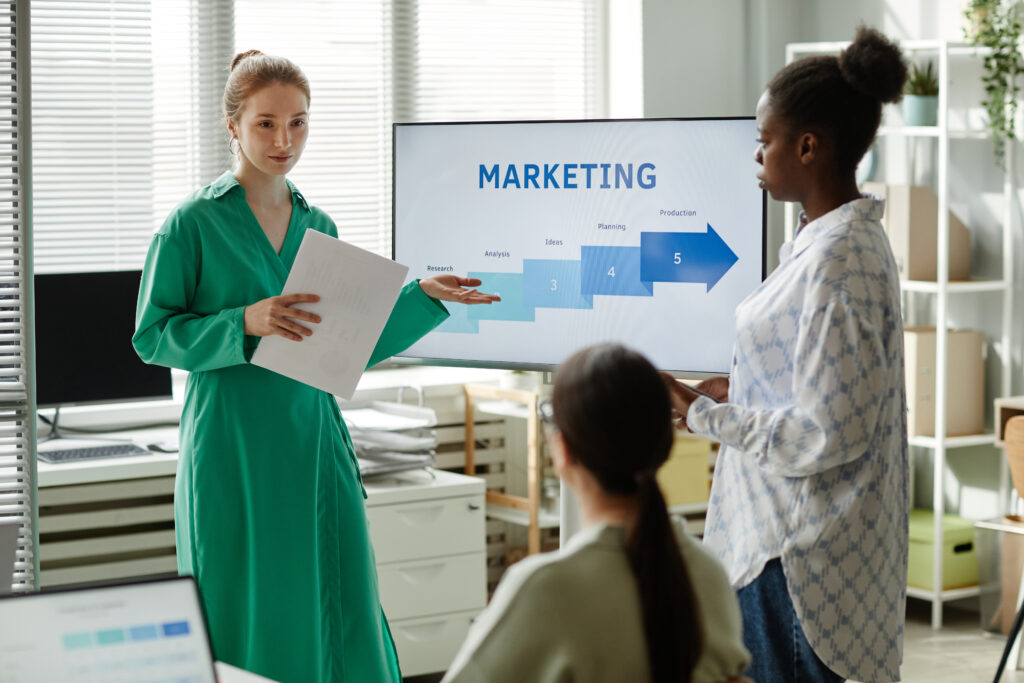 Young businesswoman with report pointing at screen with graphs and giving new information to her colleagues at training