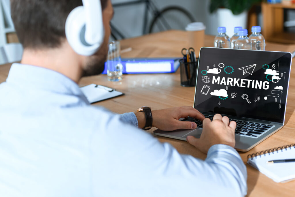 cropped shot of businessman in headphones listening music and working at laptop with marketing word, online masters degree in marketing