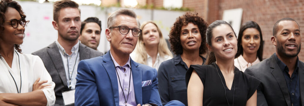Group Of Businessmen And Businesswomen Listening To Presentation At Conference