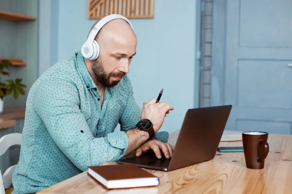 An adult man is drinking coffee and typing on a laptop.