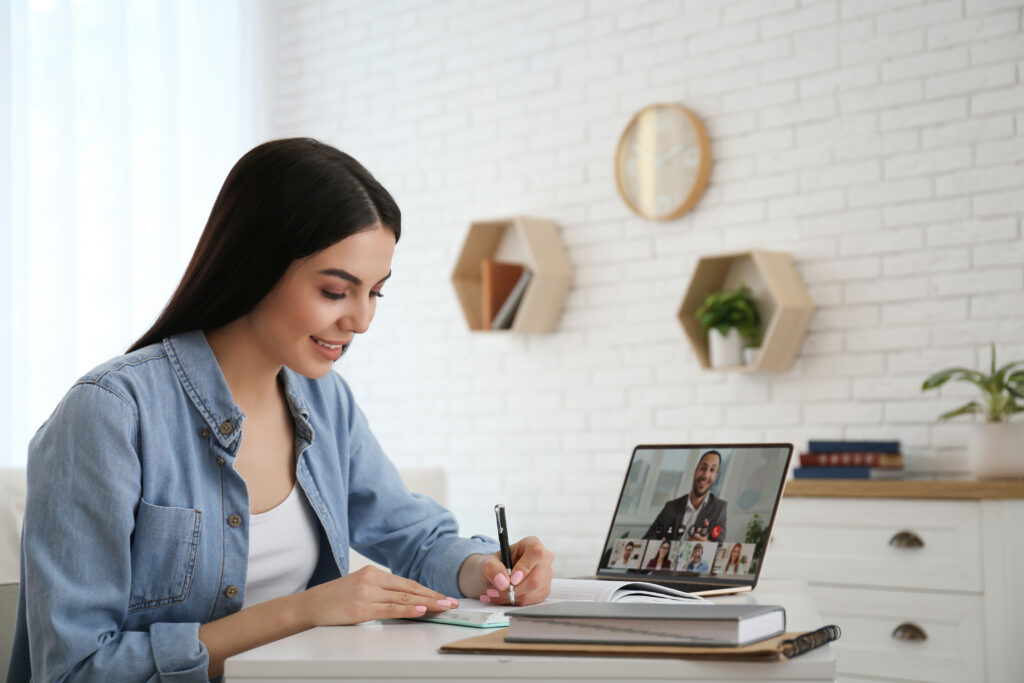 Young woman taking notes during online webinar at table indoors