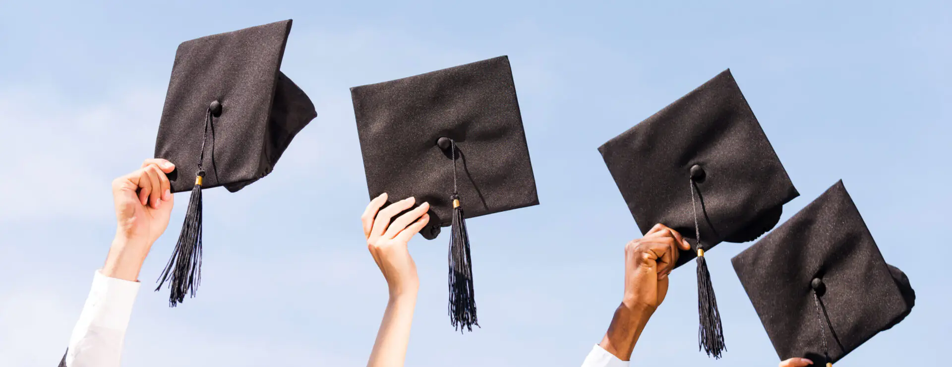 Finally graduated! Close-up of four hands holding mortar boards against sky background